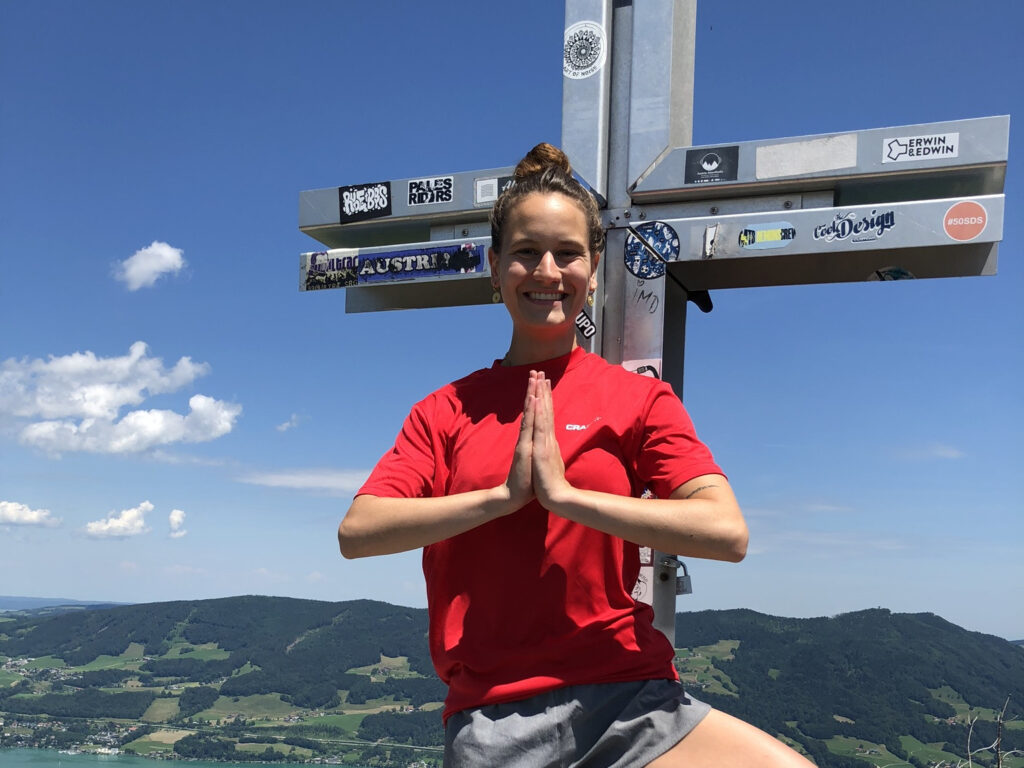 Eine junge Frau macht eine Yogapose vor einem Gipfelkreuz